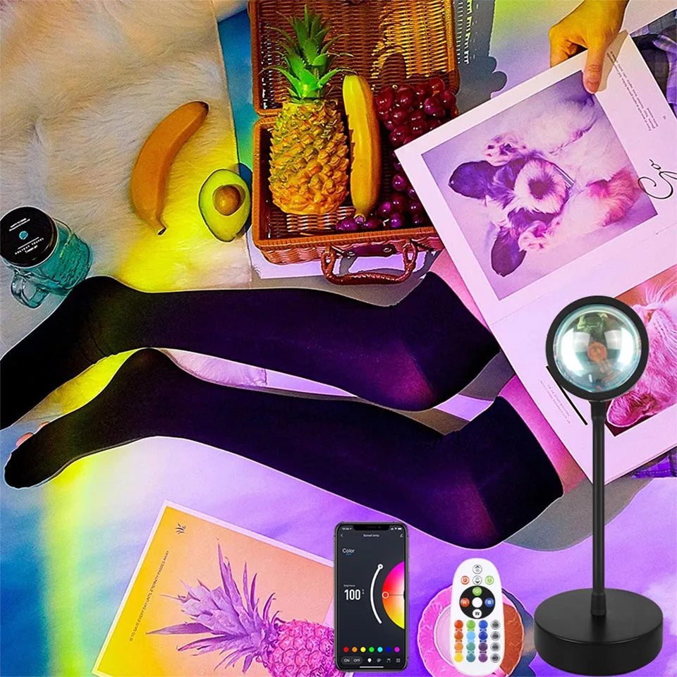 Black sunset LED projection lamp with app and remote control, casting vibrant, colourful light over a flat lay scene.