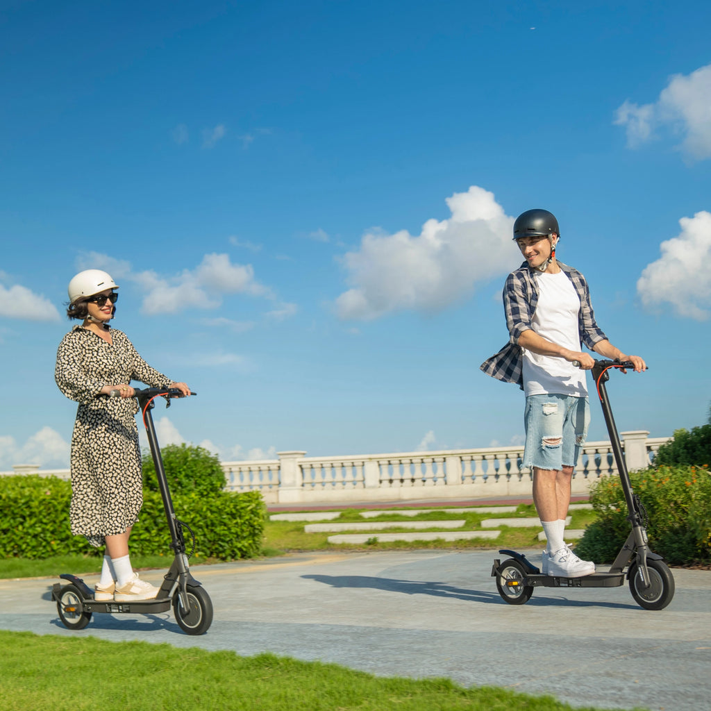 Two people ride black 5TH WHEEL V30Pro electric scooters outdoors on a paved path wearing helmets.