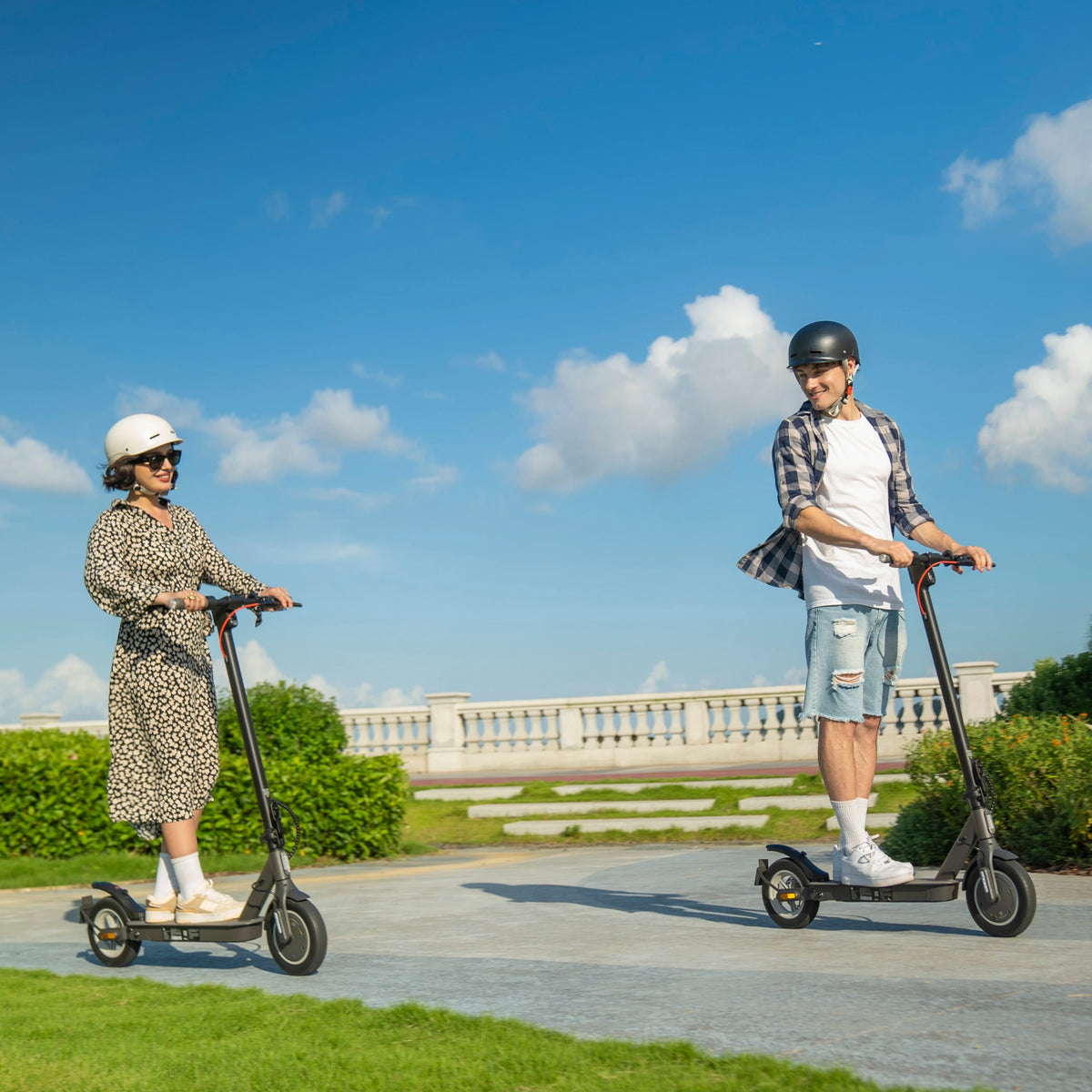 Two people ride black 5TH WHEEL V30Pro electric scooters outdoors on a paved path wearing helmets.