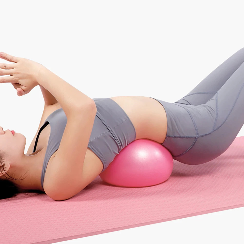 A person in grey activewear lying on a pink mat with a small, round pink pilates ball under their lower back.