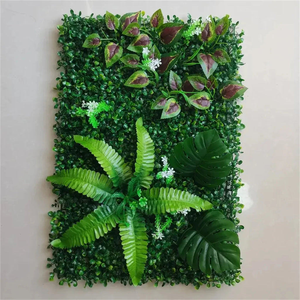 Artificial green plant wall panel featuring lush mixed foliage, including ferns, monstera leaves, and small white flowers.