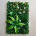 Artificial green plant wall panel featuring lush mixed foliage, including ferns, monstera leaves, and small white flowers.