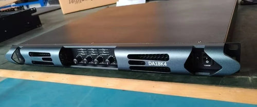 Dark grey 4-channel professional power amplifier with a sleek metal chassis, front control knobs, and air vents.