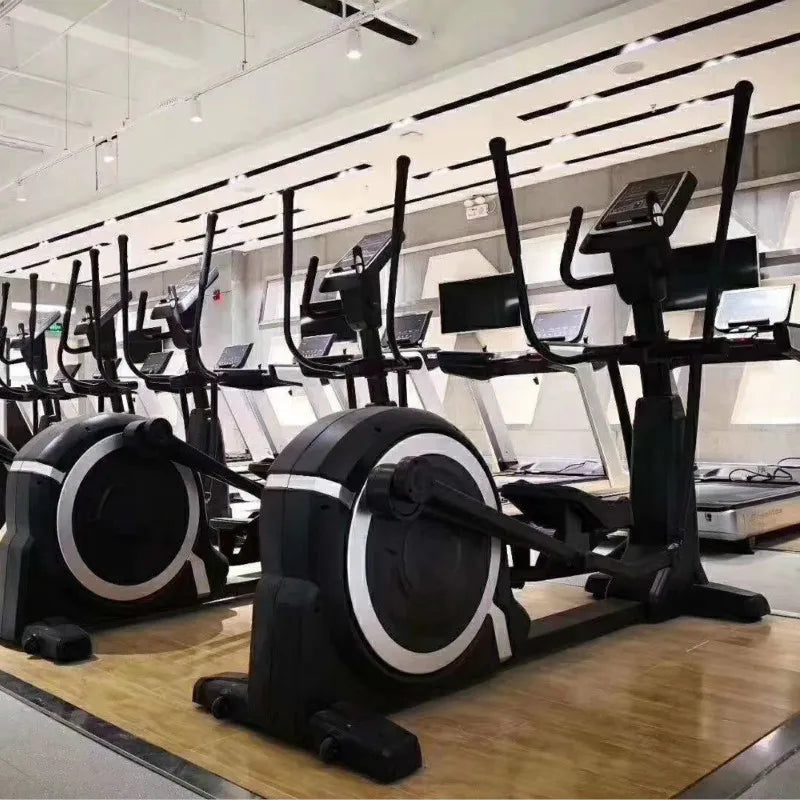 A row of black and silver commercial elliptical trainers with digital consoles in a modern gym setting.