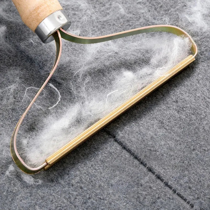 A wooden-handled metal lint remover tool collecting white fluff from a grey fabric surface.