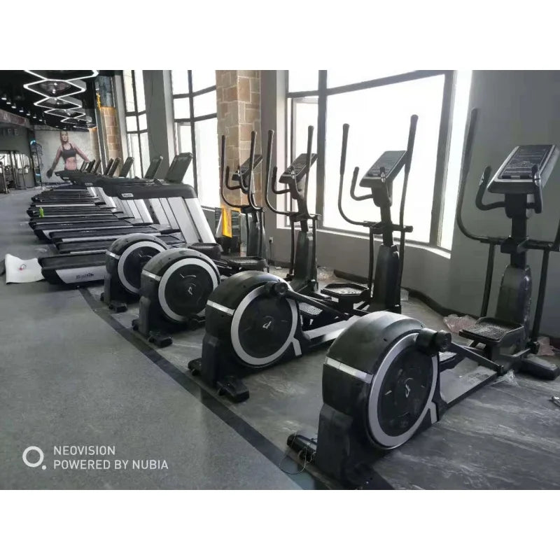 Row of professional black elliptical cross trainers with silver circular detailing, set up in a bright gym.