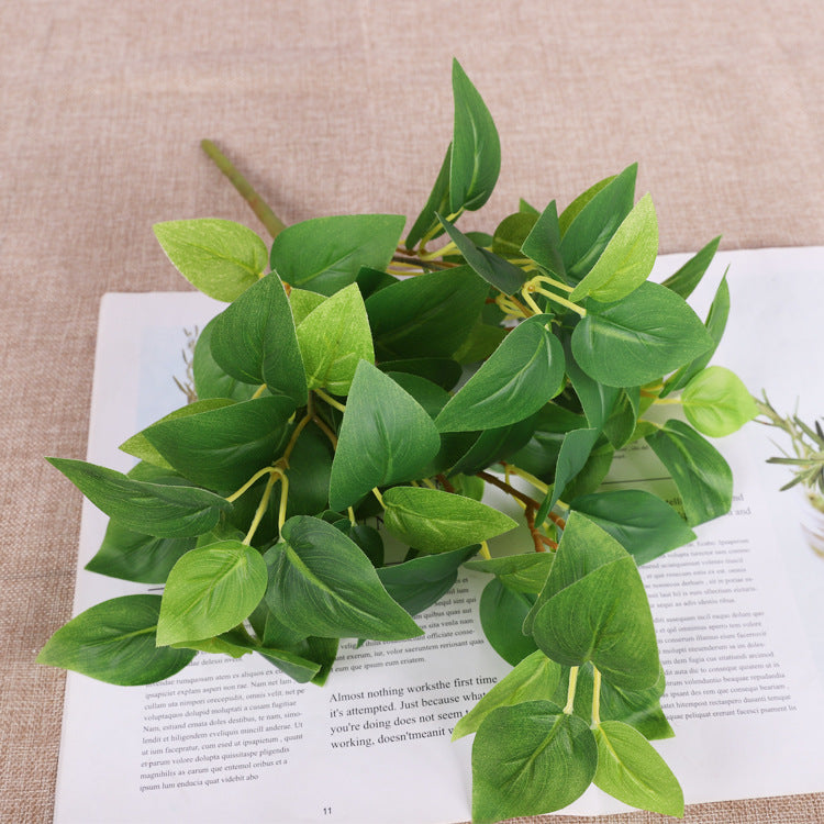 Artificial green leafy plant sprig with pointed leaves, lying on a document.