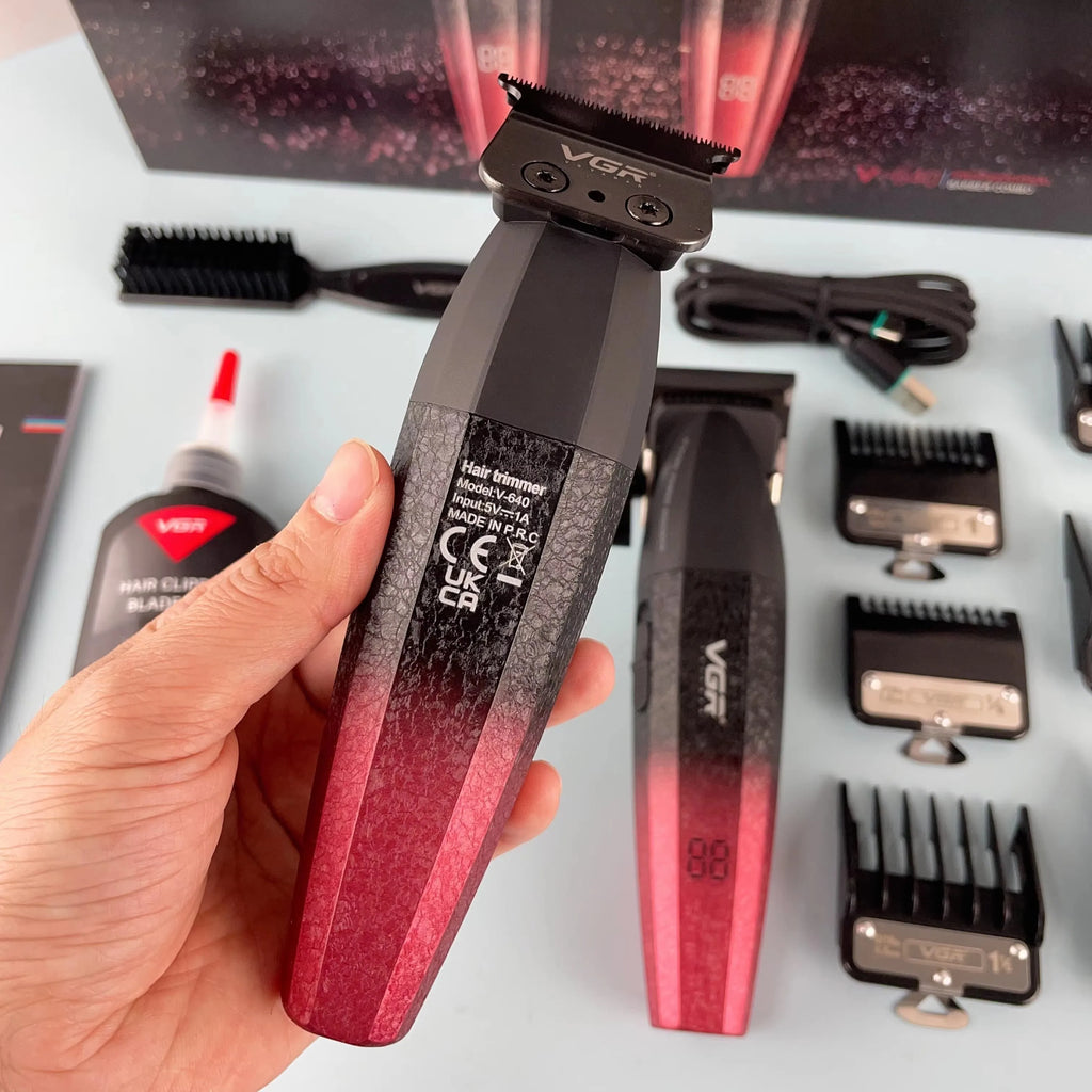 Hand holding a professional cordless hair and beard trimmer with a black-to-red gradient finish and digital display.