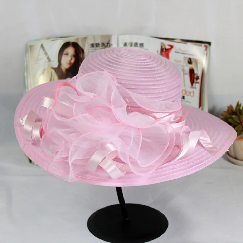 Elegant pale pink wide-brim occasion hat featuring a ruffled organza flower and satin ribbon detail.