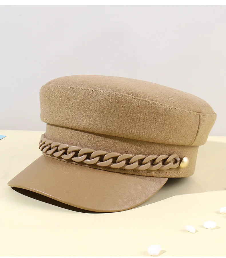 Beige felt baker boy hat with a matching plastic chain detail and a smooth, faux-leather peak.