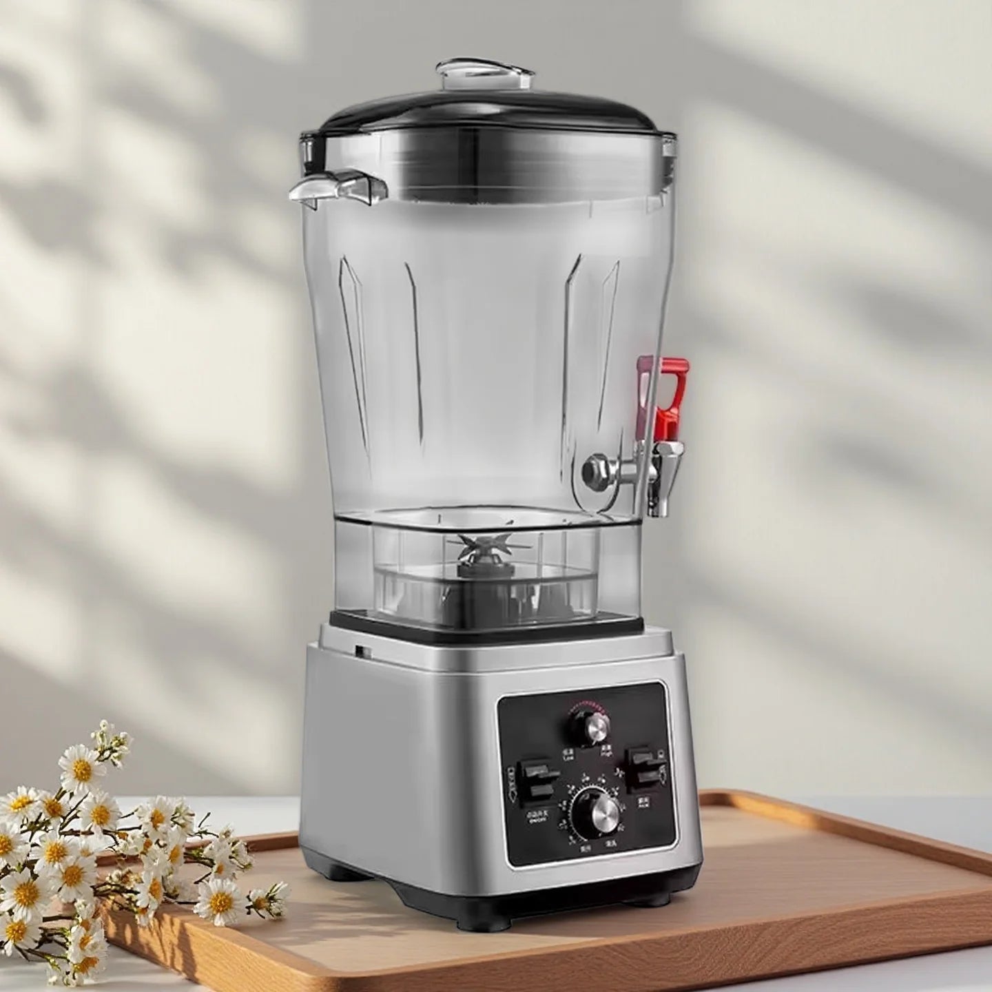 Silver commercial blender with a clear pitcher, built-in red dispenser tap, and black manual control panel base.
