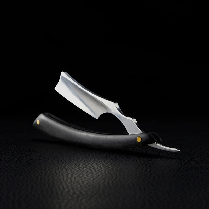 Professional stainless steel straight razor with a dark, textured handle and metallic gold detailing.