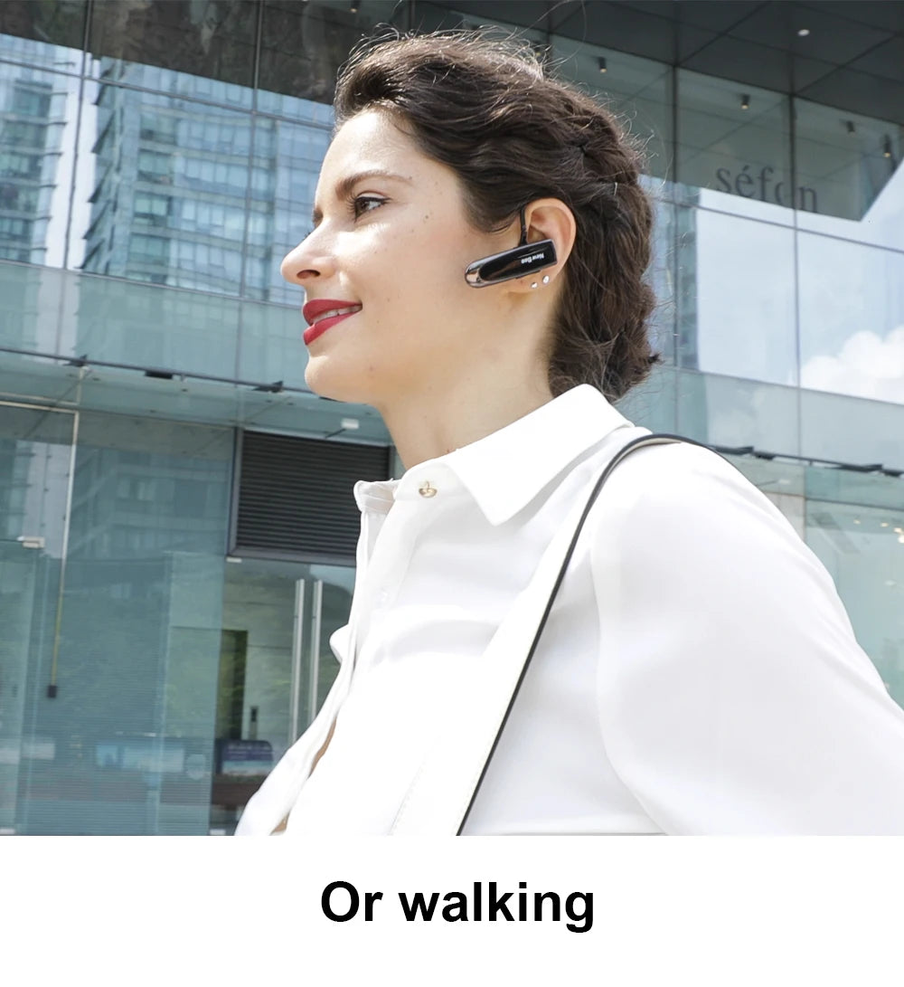A woman walking outdoors wearing a sleek, black wireless Bluetooth headset with a built-in microphone.