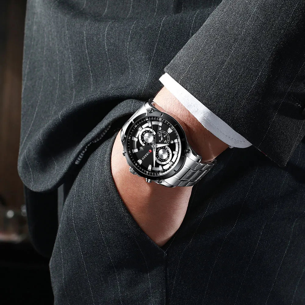 Men's luxury stainless steel wristwatch with a black chronograph dial, worn with a tailored pinstripe business suit.