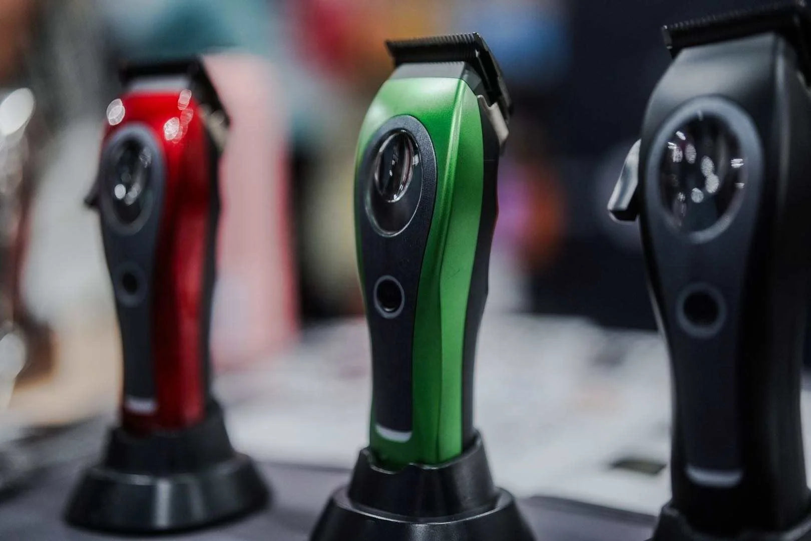 Three cordless hair clippers in red, green, and black standing in individual charging docks.