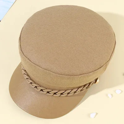 Beige felt baker boy hat with a matching faux-leather peak and decorative braided chain trim.
