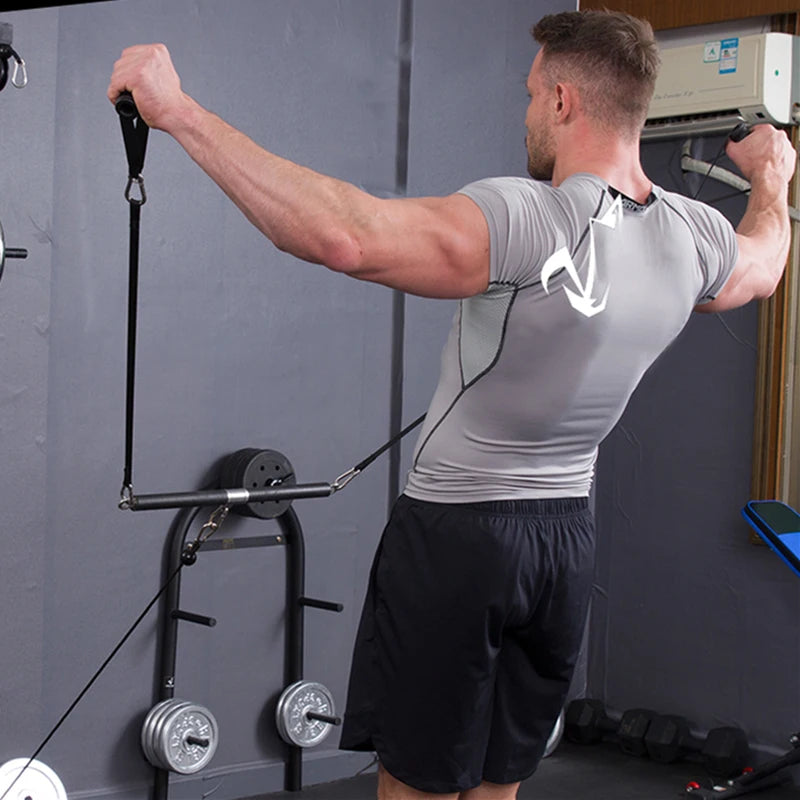 A man in a grey athletic shirt and black shorts exercises using a black cable machine with resistance bands.