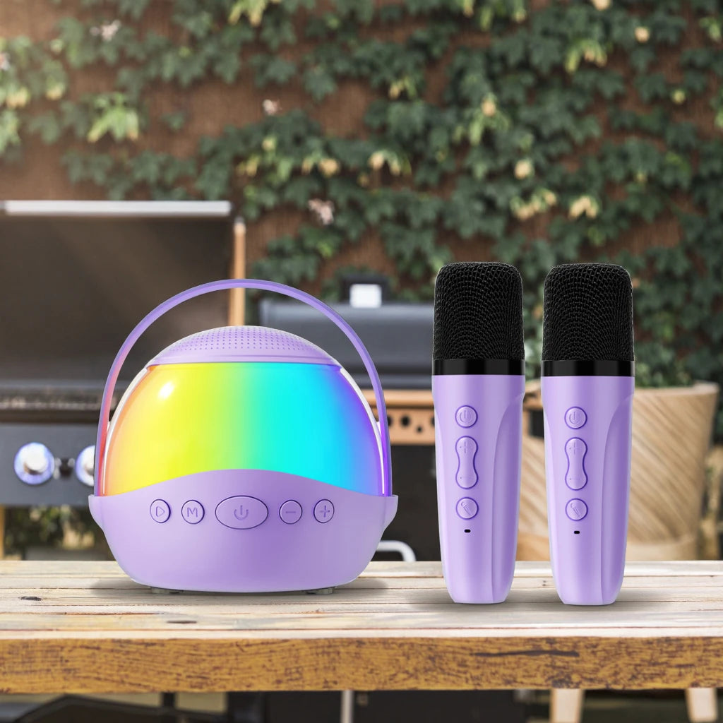 Lilac wireless karaoke speaker with rainbow LED light and two matching handheld microphones on a wooden table.