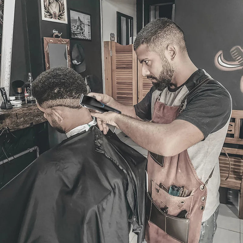 A barber using a sleek, black rechargeable electric hair trimmer to style a client's hair in a salon setting.