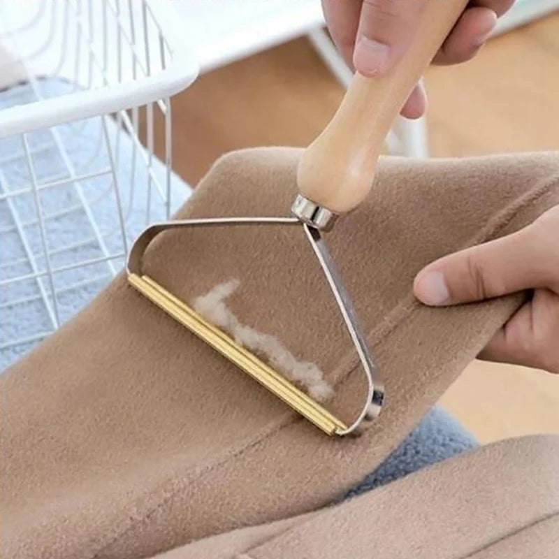 Handheld fabric shaver with a wooden handle and metal blade removing lint from a beige woollen garment.