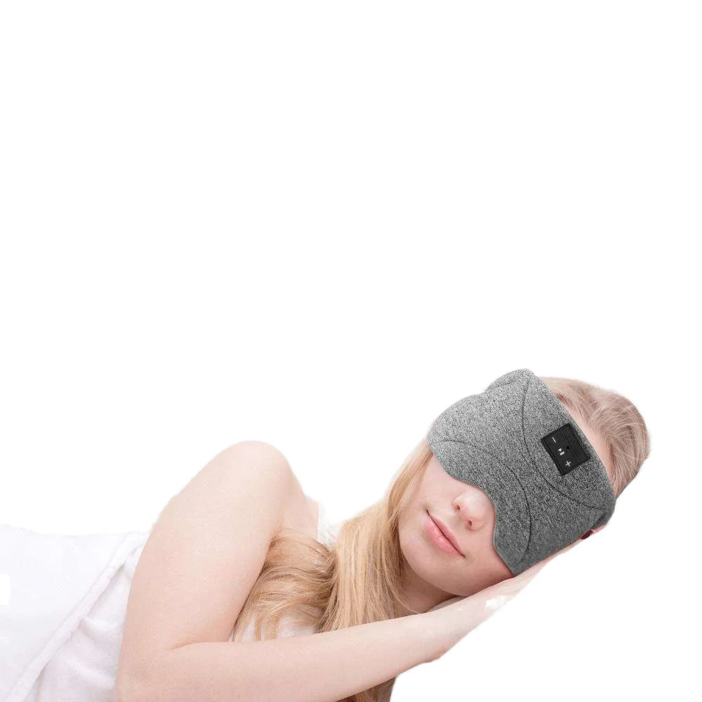 Woman wearing a soft grey wireless Bluetooth sleep eye mask with built-in control panel for headphones.