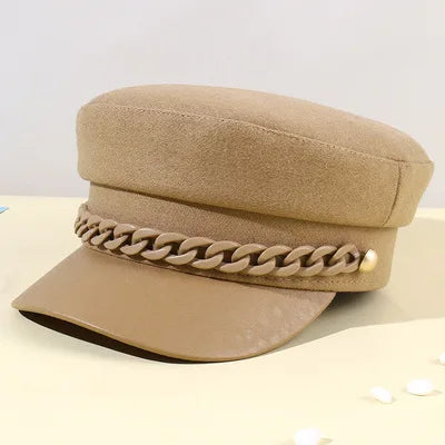 Tan felt baker boy hat with a matching plastic chain detail and a smooth, tonal peak.