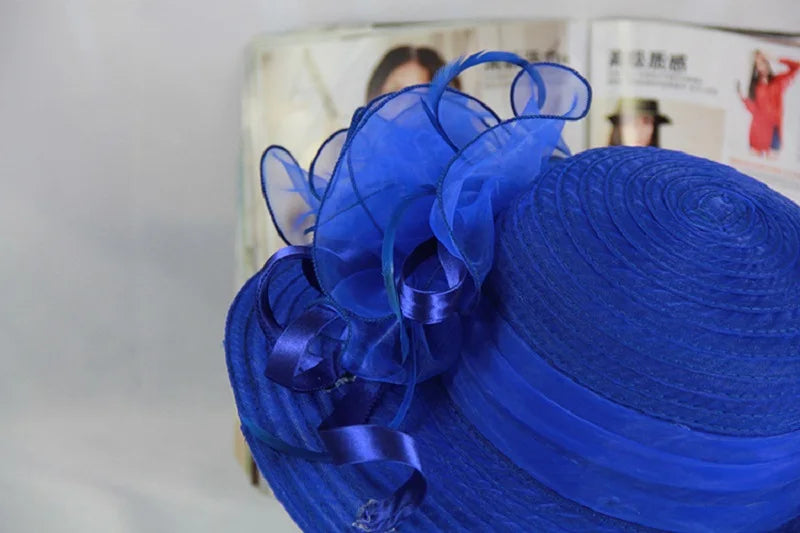 A vibrant royal blue occasion hat featuring a wide brim, a satin band, and a decorative organza floral accent.