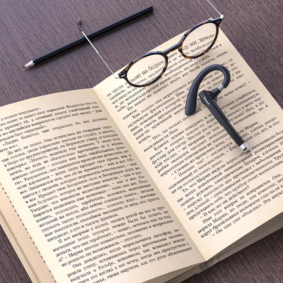 Sleek, black wireless Bluetooth headphones with a microphone resting on an open book next to reading glasses.