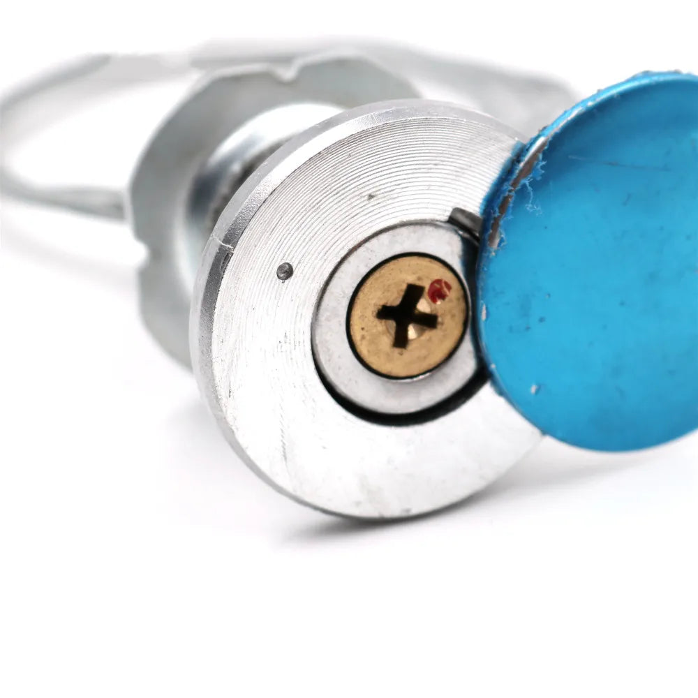 Silver metal door lock cylinder with a gold-tone screw center and a small blue circular protective sticker.