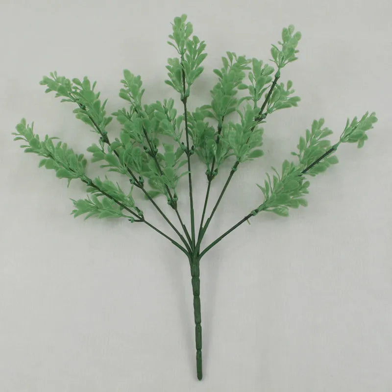 An artificial plastic plant stem with light green, fern-like leaves branching out from a single base.