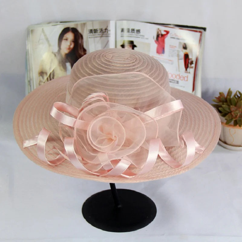 Elegant pale pink wide-brim occasion hat featuring a sheer organza floral trim and satin ribbon detailing.