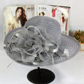 Grey wide-brim occasion hat featuring a large, ruffled organza flower and satin ribbon detailing.