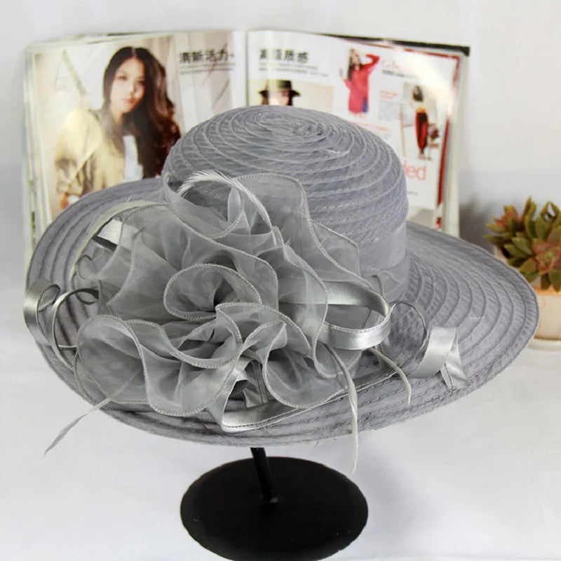 Grey wide-brim occasion hat featuring a large, ruffled organza flower and satin ribbon detailing.