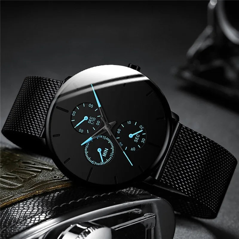 Ultra-thin men's watch with a black dial, stainless steel mesh strap, and luminous blue accents on the sub-dials.