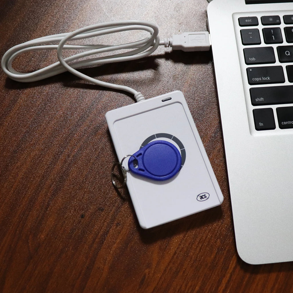 White plastic RFID card reader with a blue key fob, plugged into a laptop via a white USB cable.