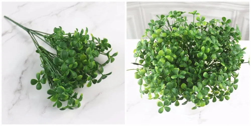 A bundle of artificial green four-leaf clover-style plants shown flat and arranged in a pot on a white marble surface.