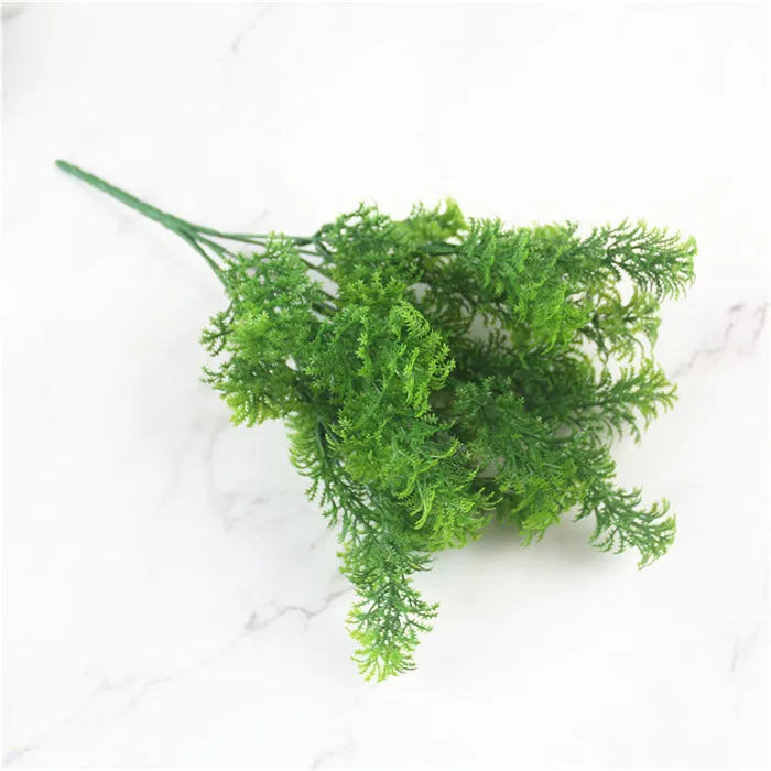 A sprig of artificial bright green fern foliage with delicate, feathery leaves on a white marble background.