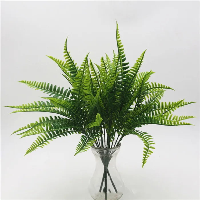 A bunch of vibrant green artificial fern leaves arranged in a clear glass vase against a plain white background.
