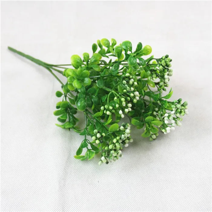 Artificial green plant sprig with small, rounded leaves and tiny white flower buds, set against a white background.