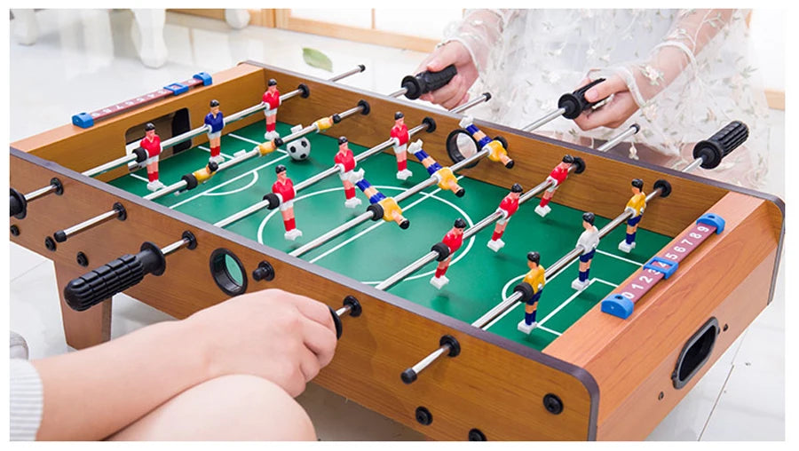 Tabletop foosball game with wood-effect finish, green pitch, metal rods, and manual sliding scorekeepers.