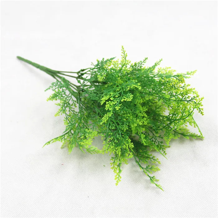 A sprig of artificial bright green fern with delicate, feathery leaves on a single stem against a white background.