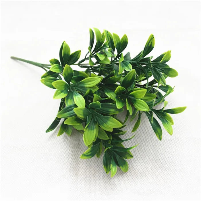 A bunch of artificial green shrub stems with layered, pointed leaves in shades of bright and dark olive green.