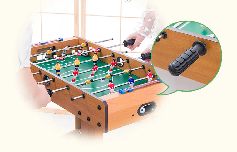 Wood-finish foosball table with players in red and yellow kits, featuring a close-up of the textured control handles.