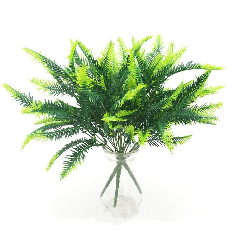 A bouquet of artificial fern fronds featuring gradient lime and dark green leaves in a clear glass vase.