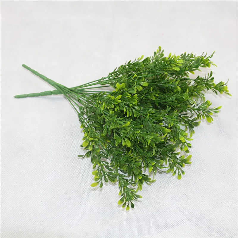 A cluster of artificial green plastic fern-like stems with small, realistic leaves on a white background.