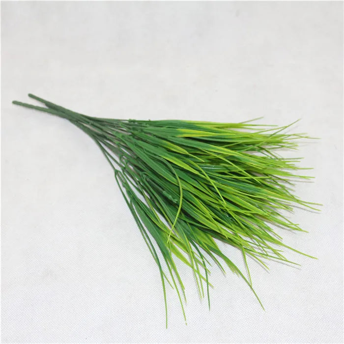 A bundle of artificial grass stems featuring long, thin green leaves with yellow-tipped highlights on a white surface.