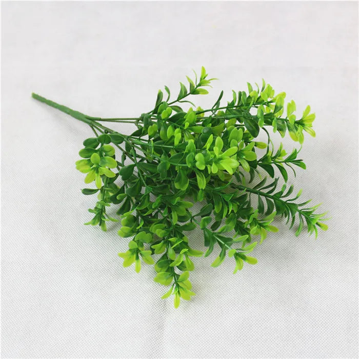 A bundle of vibrant green artificial boxwood sprigs with small, delicate leaves against a plain white background.