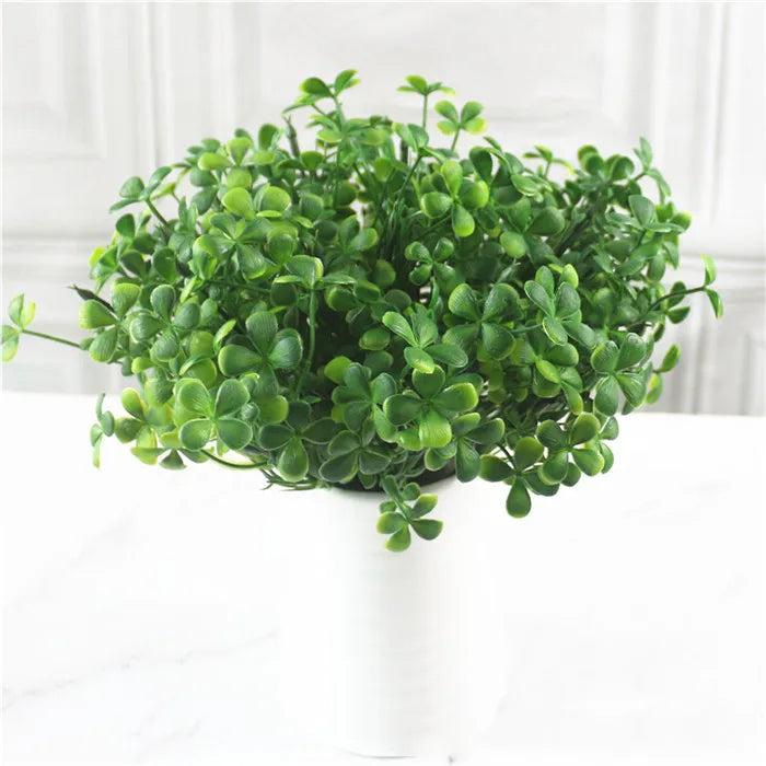 A bushy artificial clover plant with vibrant green leaves in a simple white vase against a white background.