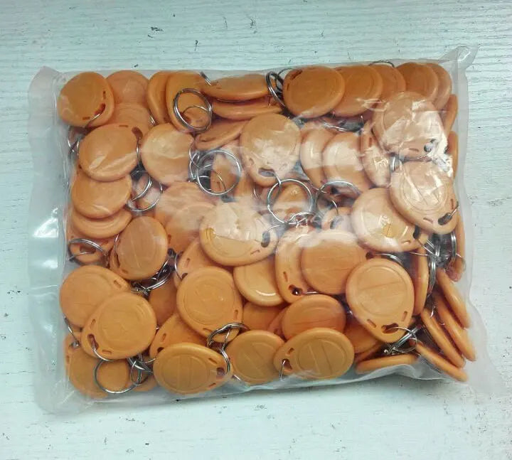 A plastic bag filled with round, orange RFID key fob tags, each attached to a small metal split ring.