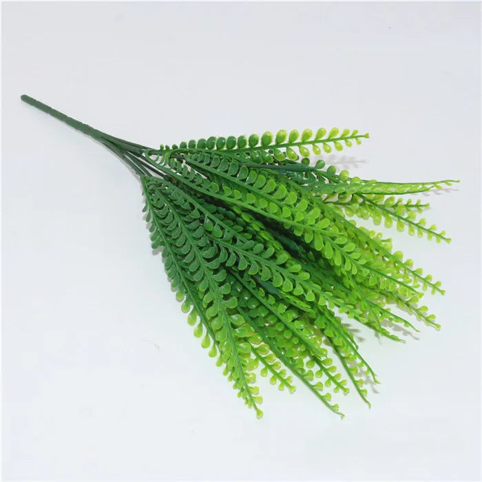 Artificial fern spray with vibrant green plastic leaves, fanning out from a single stem against a plain white background.